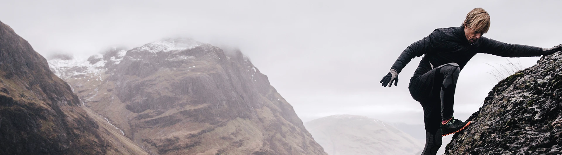Man climbing a rock with foggy mountain view in the background (photo)