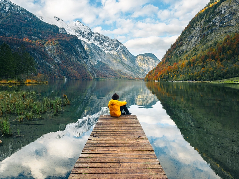 Person sitting on a wooden pier, looking out over a calm mountain lake. (photo)