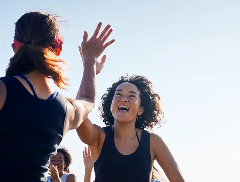 Two women smiling and giving each other a high five outdoors. (photo)