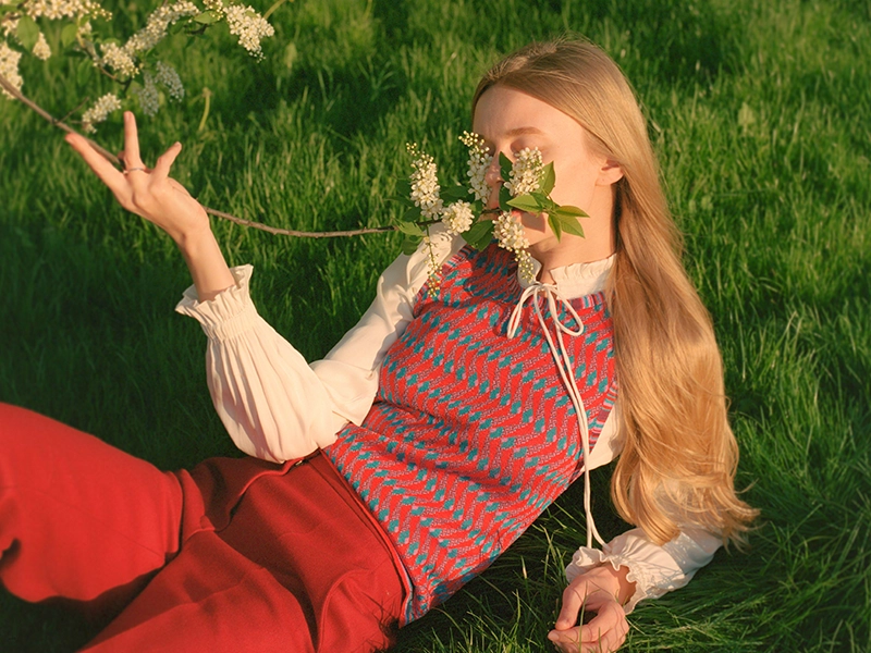 A young woman lies on green grass in warm sunlight, holding a flowering branch over her face. (photo)