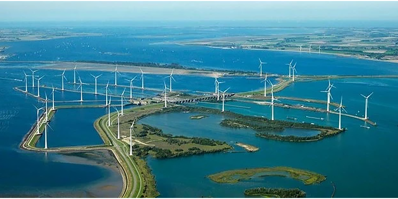 Wind turbines installed across a landscape with water. (photo)