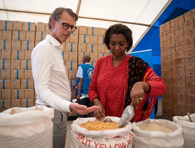 Our ongoing partnership with the WFP. Dimitri de Vreeze, Chief Executive Officer, and a woman inspecting bags of grain inside a warehouse or relief tent. (photo)