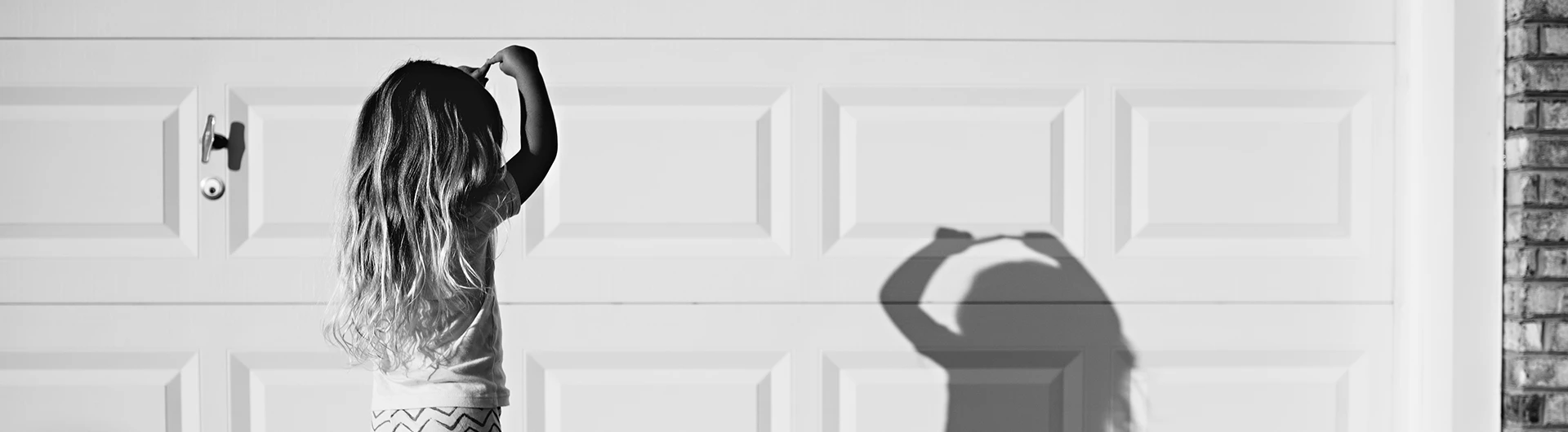 A child standing in front of a garage door, seen from behind. (photo)