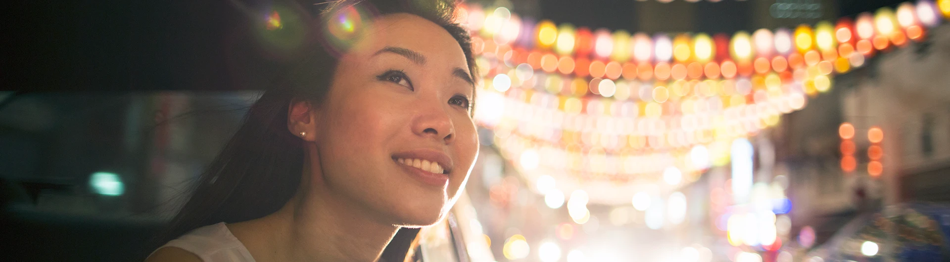 A person looking out at colorful lights at night, smiling slightly. (photo)