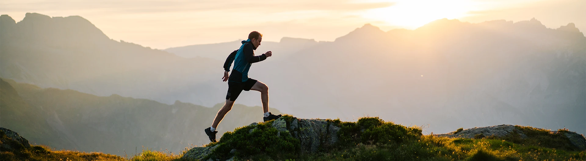 A runner moves uphill along a mountain ridge at sunrise, with layered peaks glowing softly in the background. (photo)