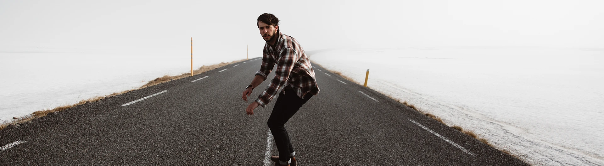 A man balances on a long, empty road stretching through a stark, snowy landscape under a pale sky. (photo)
