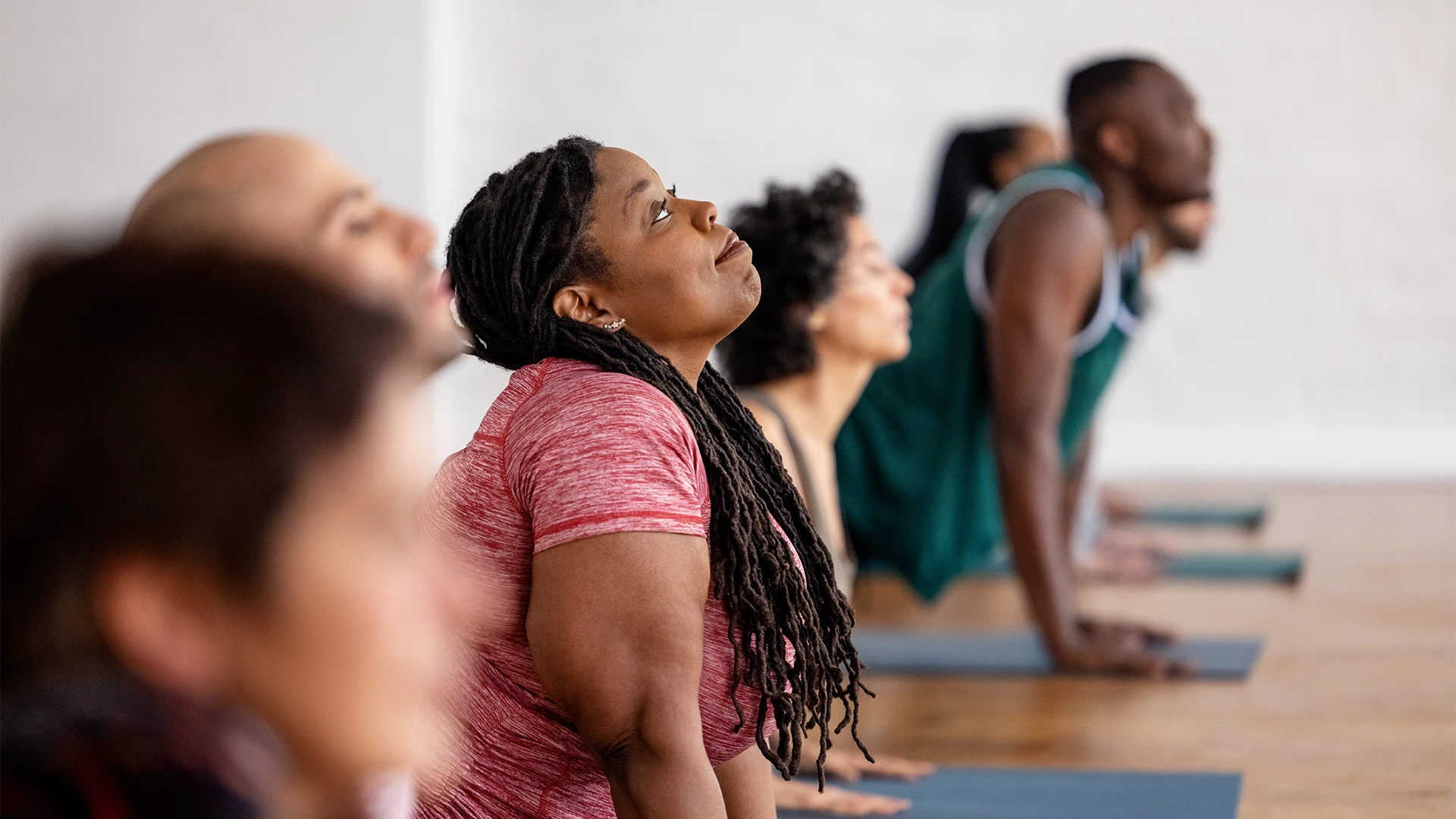 A group of people practice yoga together in a studio, holding an upward-facing pose on their mats. (photo)