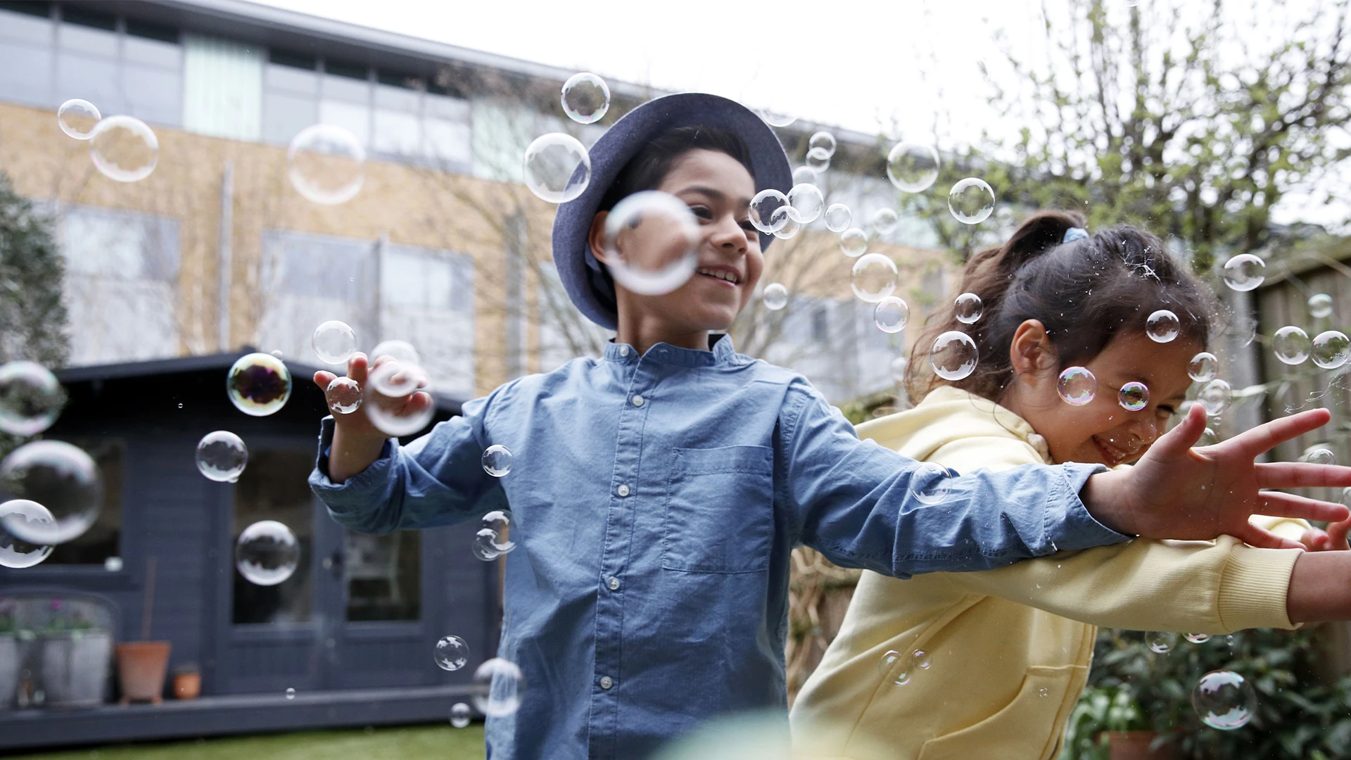 Two children laugh and reach for floating soap bubbles in a garden courtyard. (photo)