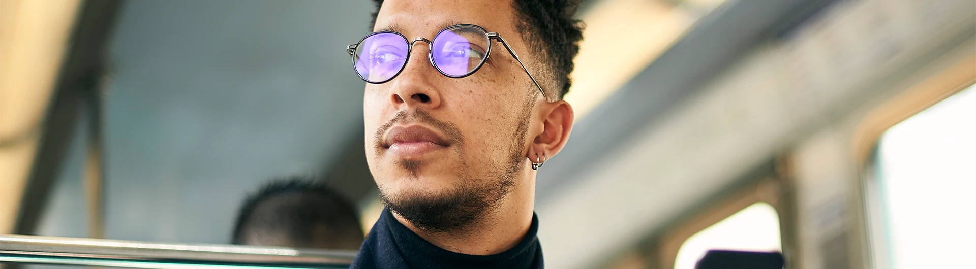 A man wearing round glasses looks out thoughtfully while riding on public transportation. (photo)