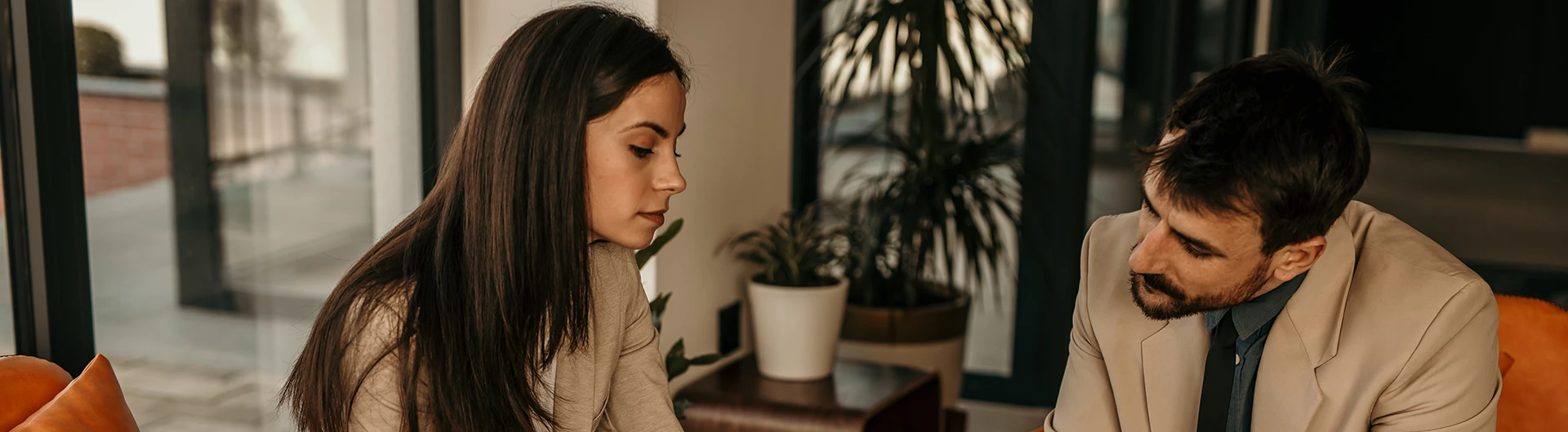 A woman and a man sit together indoors, looking down as they review something on a table. (photo)