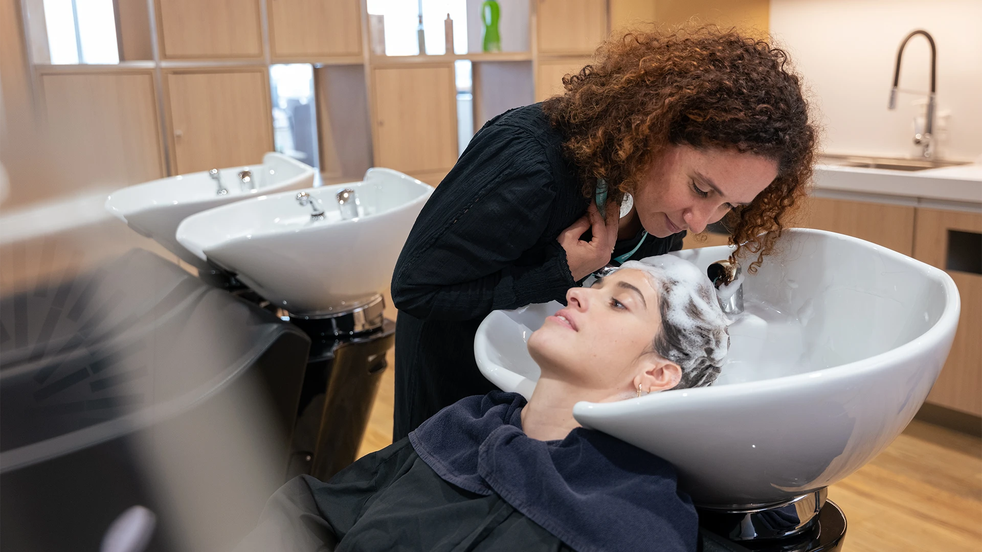 A hairstylist gently washes a client’s hair at a modern salon sink. (photo)