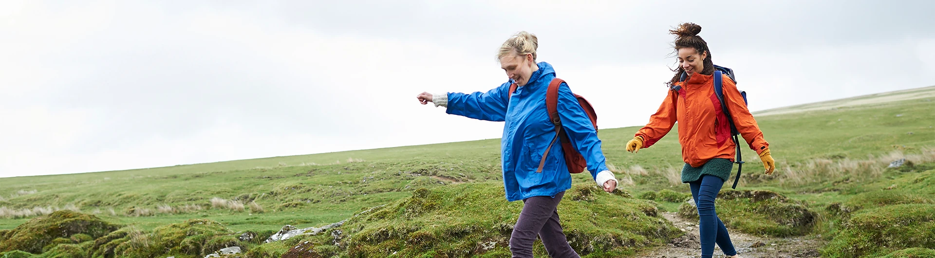 Two people wearing backpacks walk across a grassy landscape. (photo)