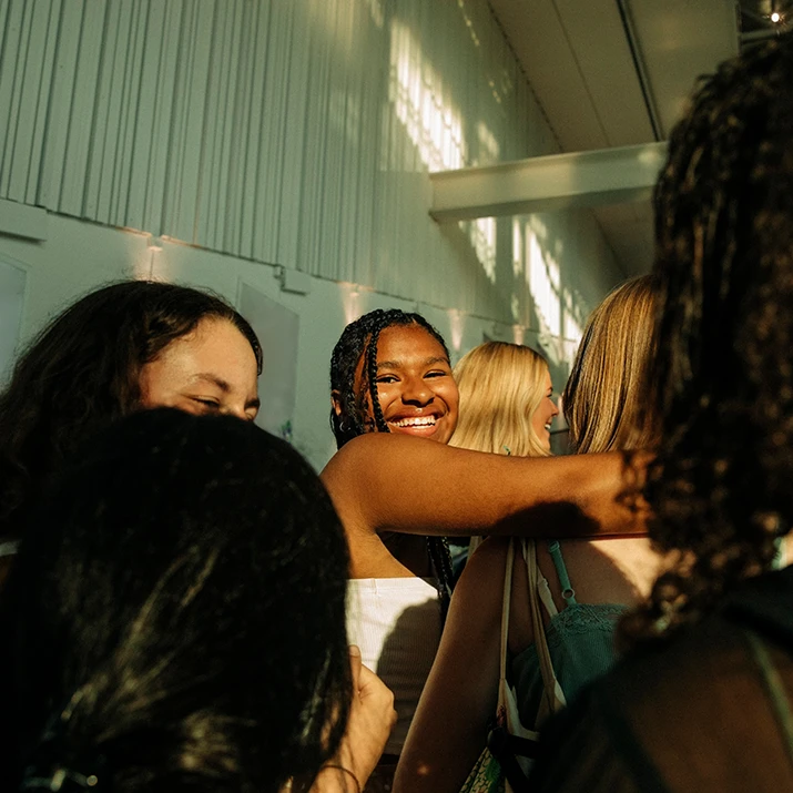 A diverse group of women stand closely together indoors, smiling and sharing a joyful moment. (photo)