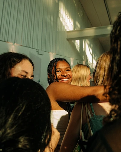 A diverse group of women stand closely together indoors, smiling and sharing a joyful moment. (photo)