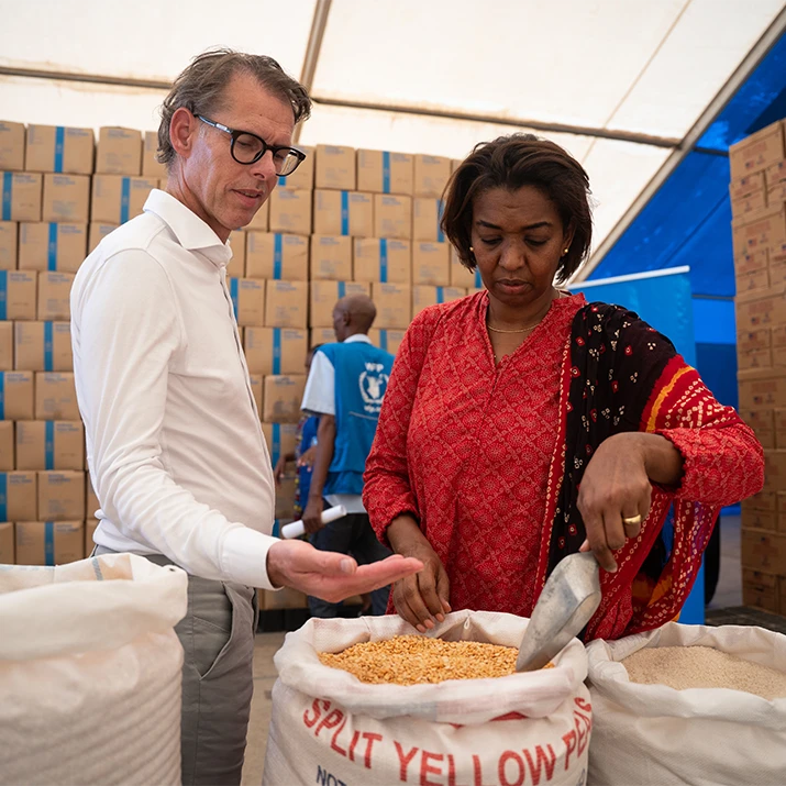 Our ongoing partnership with the WFP. Dimitri de Vreeze, Chief Executive Officer, and a woman inspecting bags of grain inside a warehouse or relief tent. (photo)