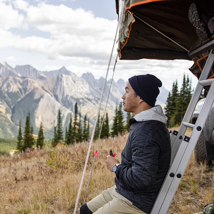 Man sitting by a camper, looking out at mountain scenery. (photo)