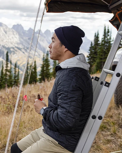 Man sitting by a camper, looking out at mountain scenery. (photo)